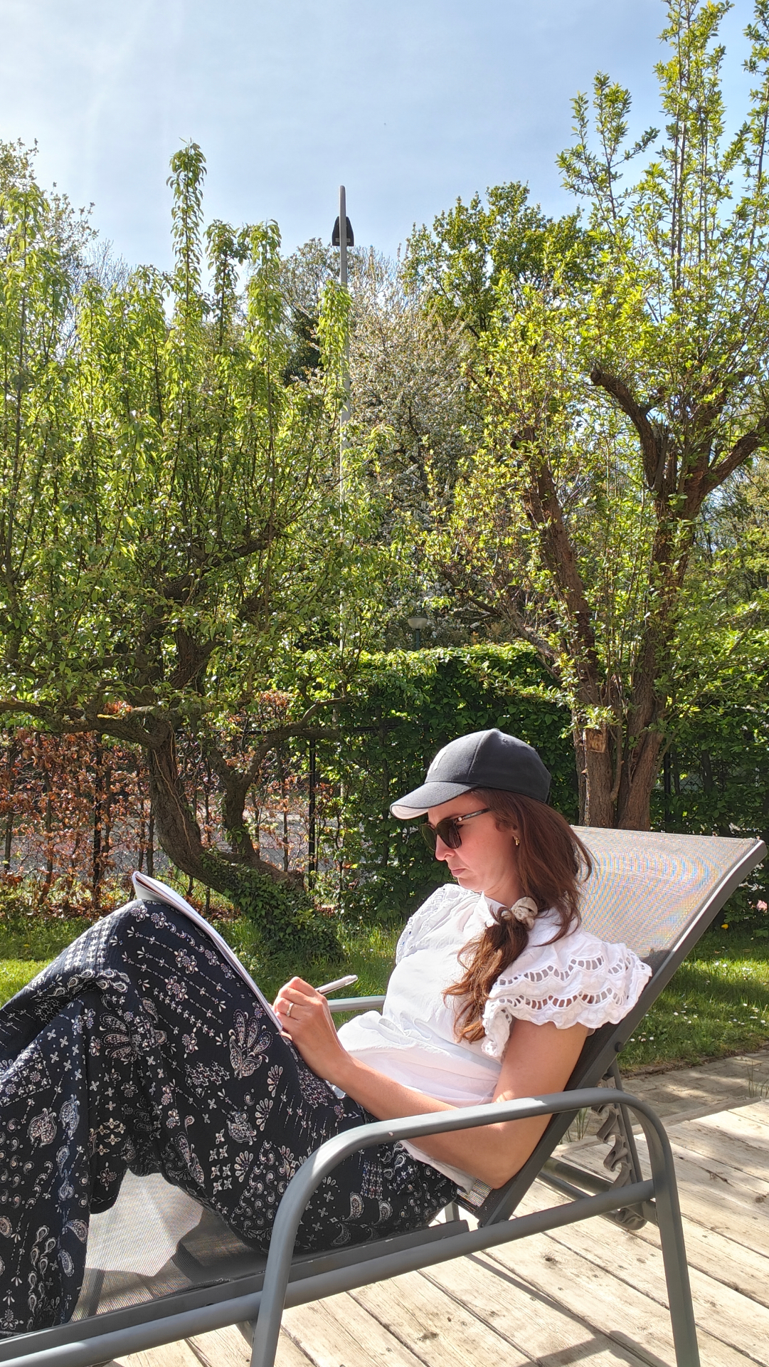 Laura sitting in a sunlit garden, writing in a notebook